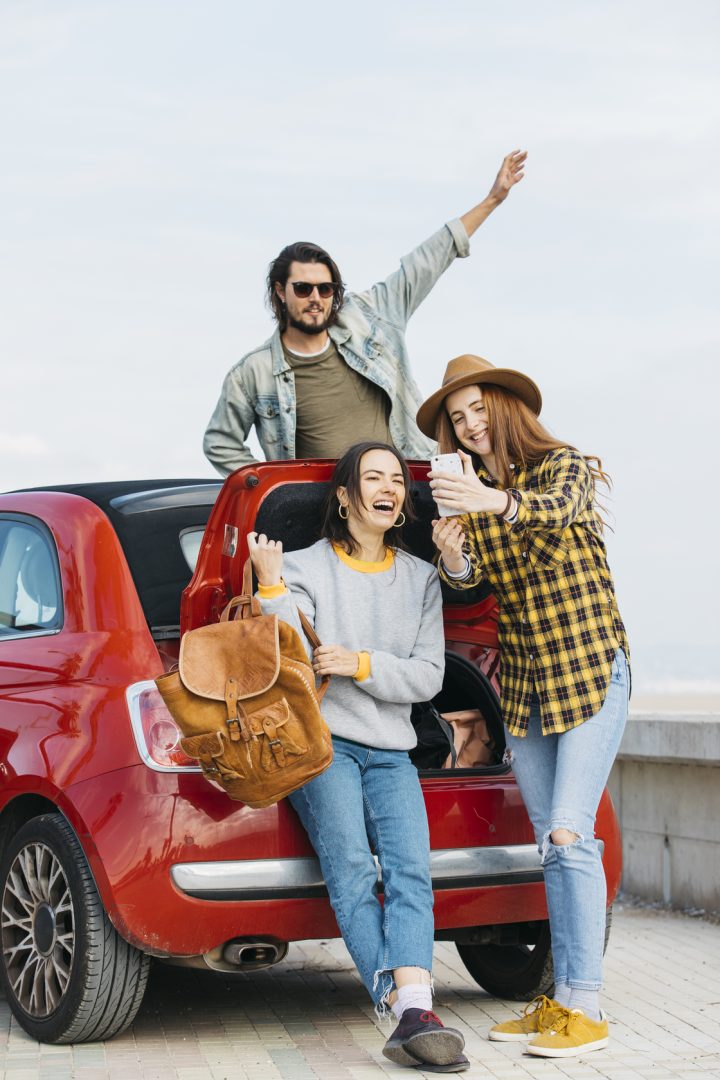 women-taking-selfie-smartphone-near-car-trunk-man-leaning-out-from-auto (2) (1)